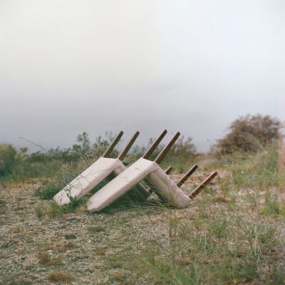 Album cover for Closeness It’s Easy by Planning for Burial, showing overturned chairs in a desolate desert setting, symbolizing isolation and emotional aftermath.